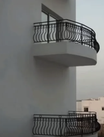 two balconies on the sides of a building - top one has doors and the bottom one is a balcony with a wall, no doors.